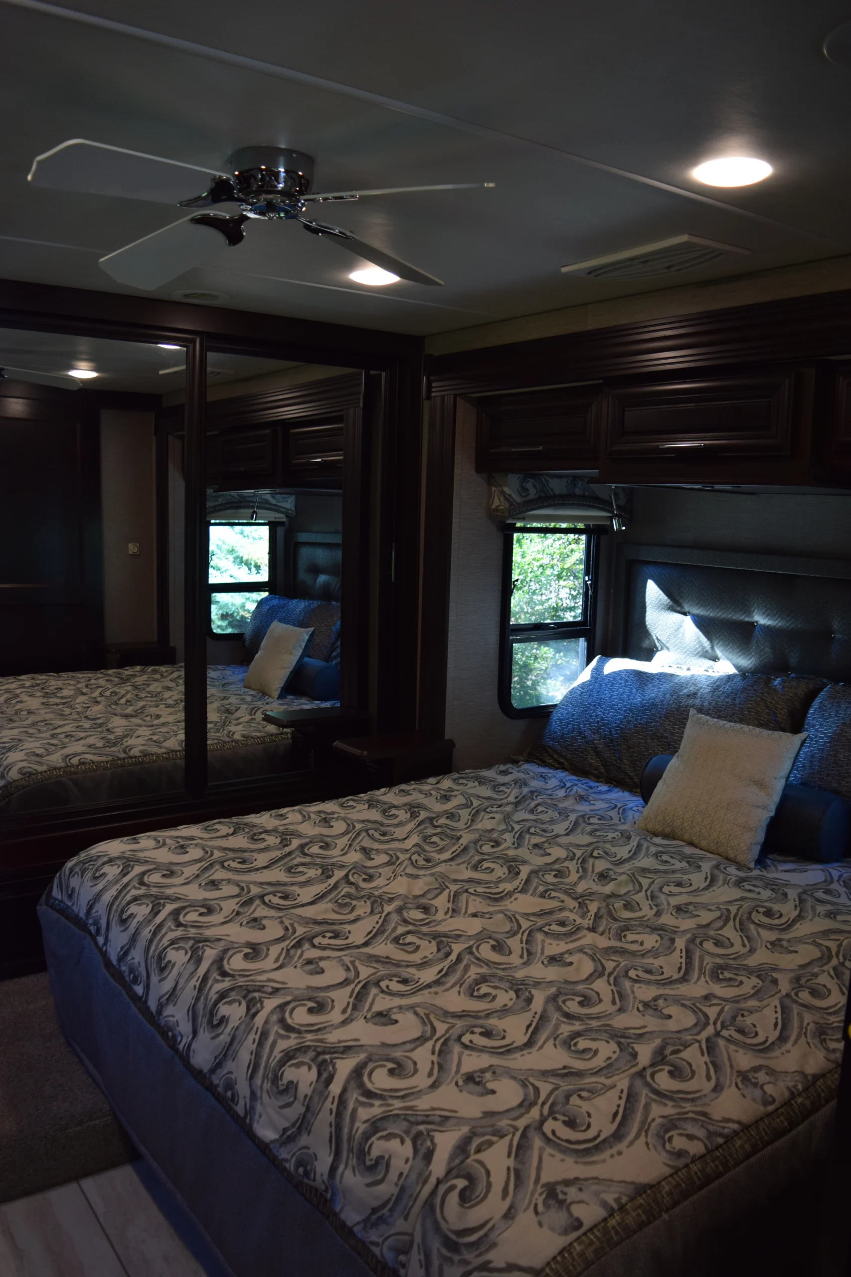 DSC_0746 Luxurious Motorcoach and Rvs bedroom featuring a patterned bedspread, overhead ceiling fan, mirrored closet, and window with scenic view.