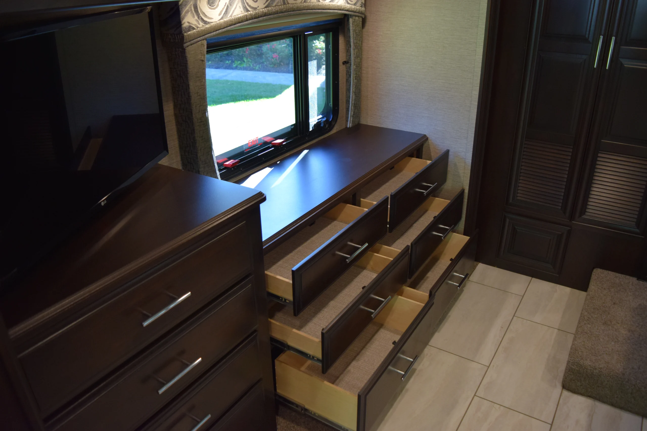 DSC_0751 Motorcoach and RVs interior featuring open dark wooden drawers under a window, next to a TV and wardrobe.