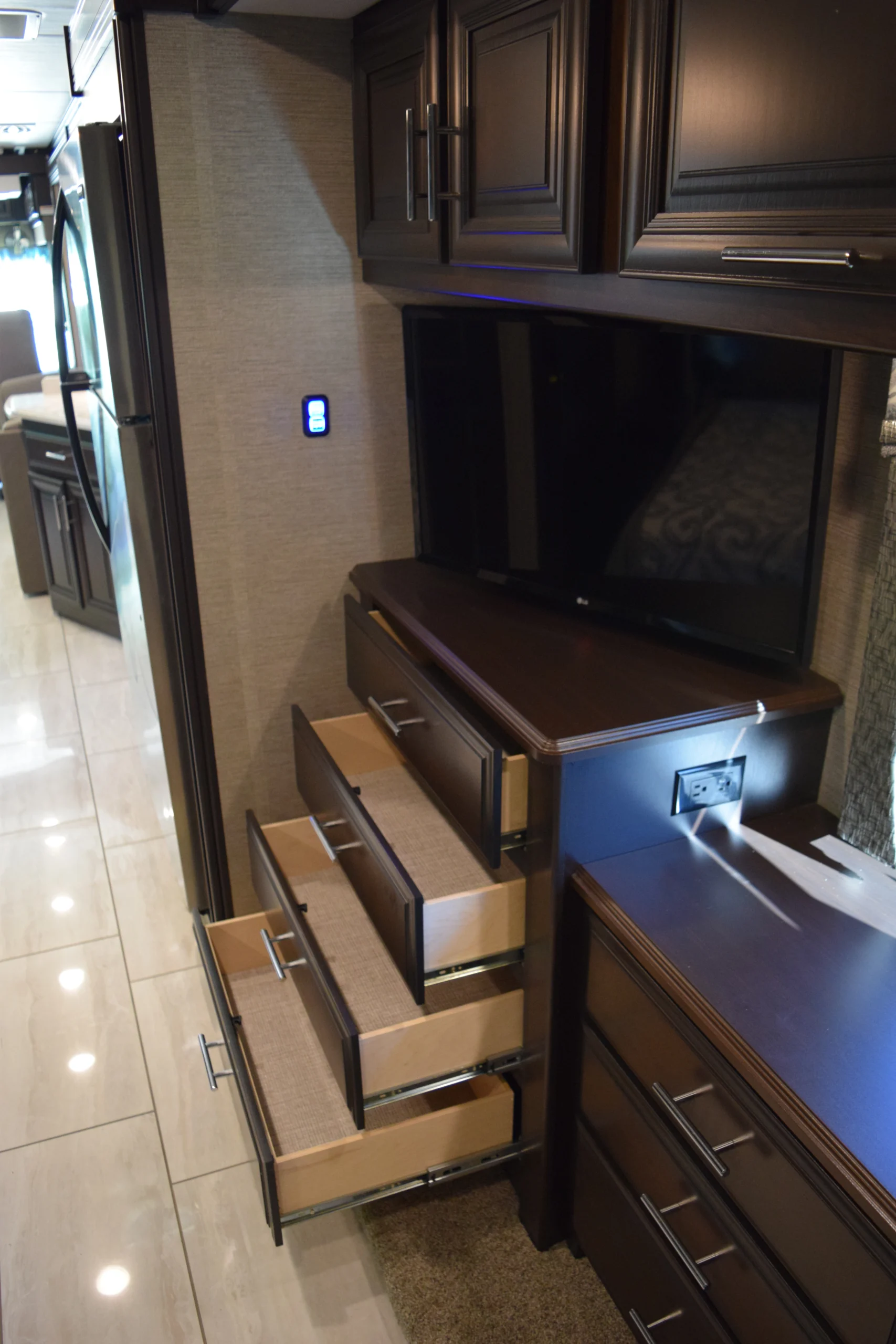 DSC_0752 Dark wood cabinetry, open drawers, and a TV in luxury Motorcoach and RV interior, highlighting modern amenities.