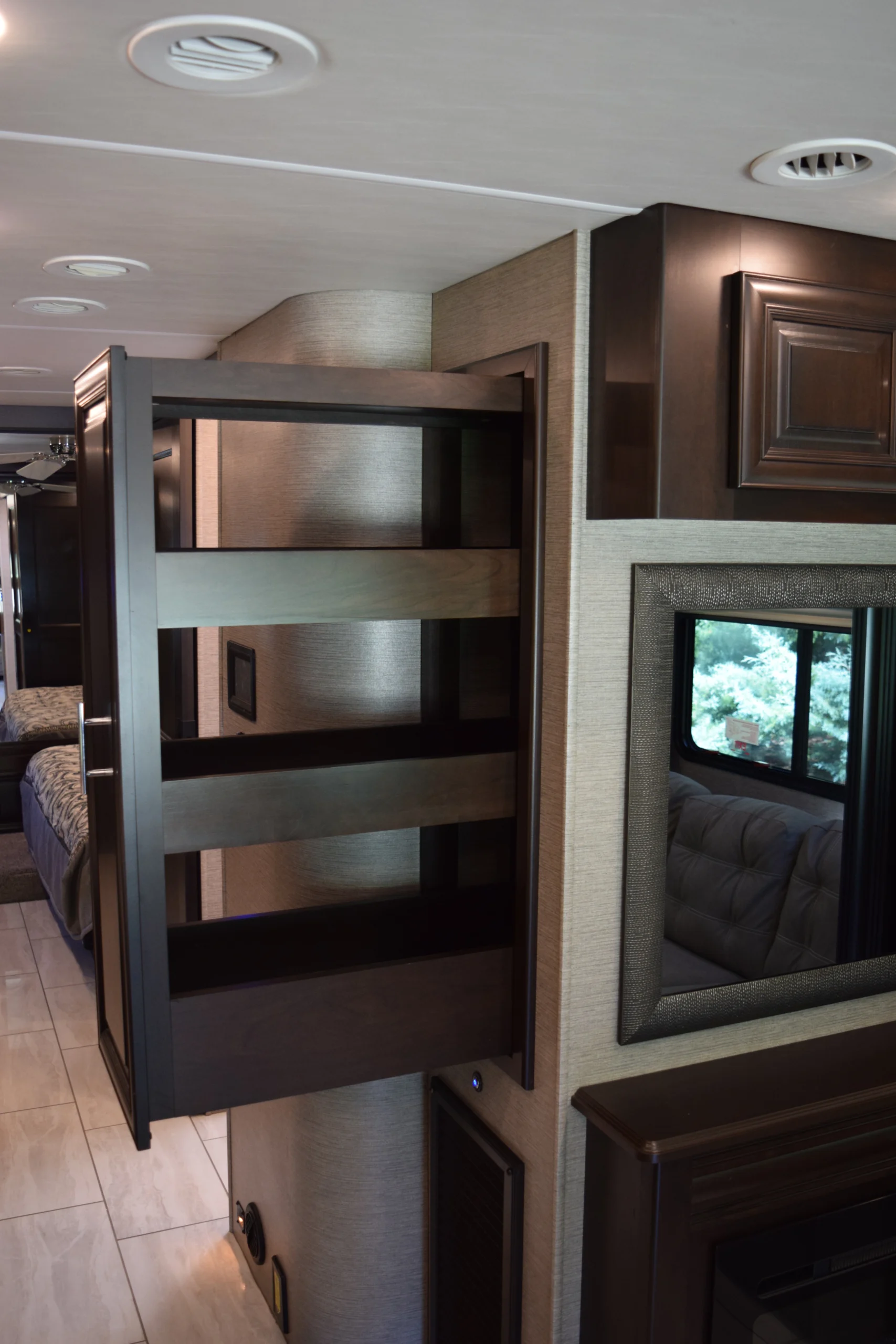 DSC_0753 Interior of a Motorcoach and RVs showcasing a pull-out pantry and modern cabinetry near a window with outdoor view.