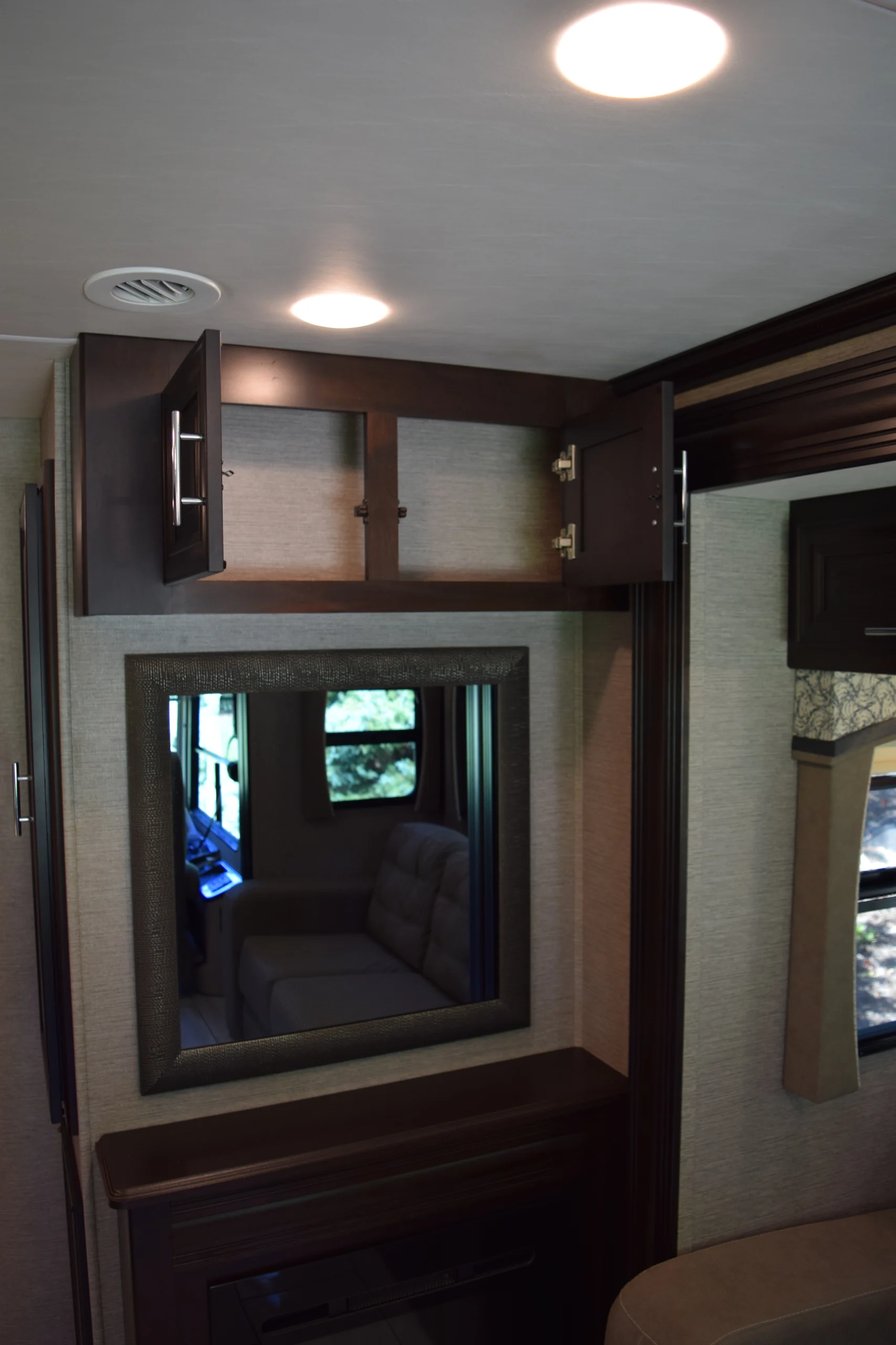 DSC_0754 Interior of a motorcoach featuring overhead cabinets, a wall mirror, and upholstered window seating reflecting through the mirror.