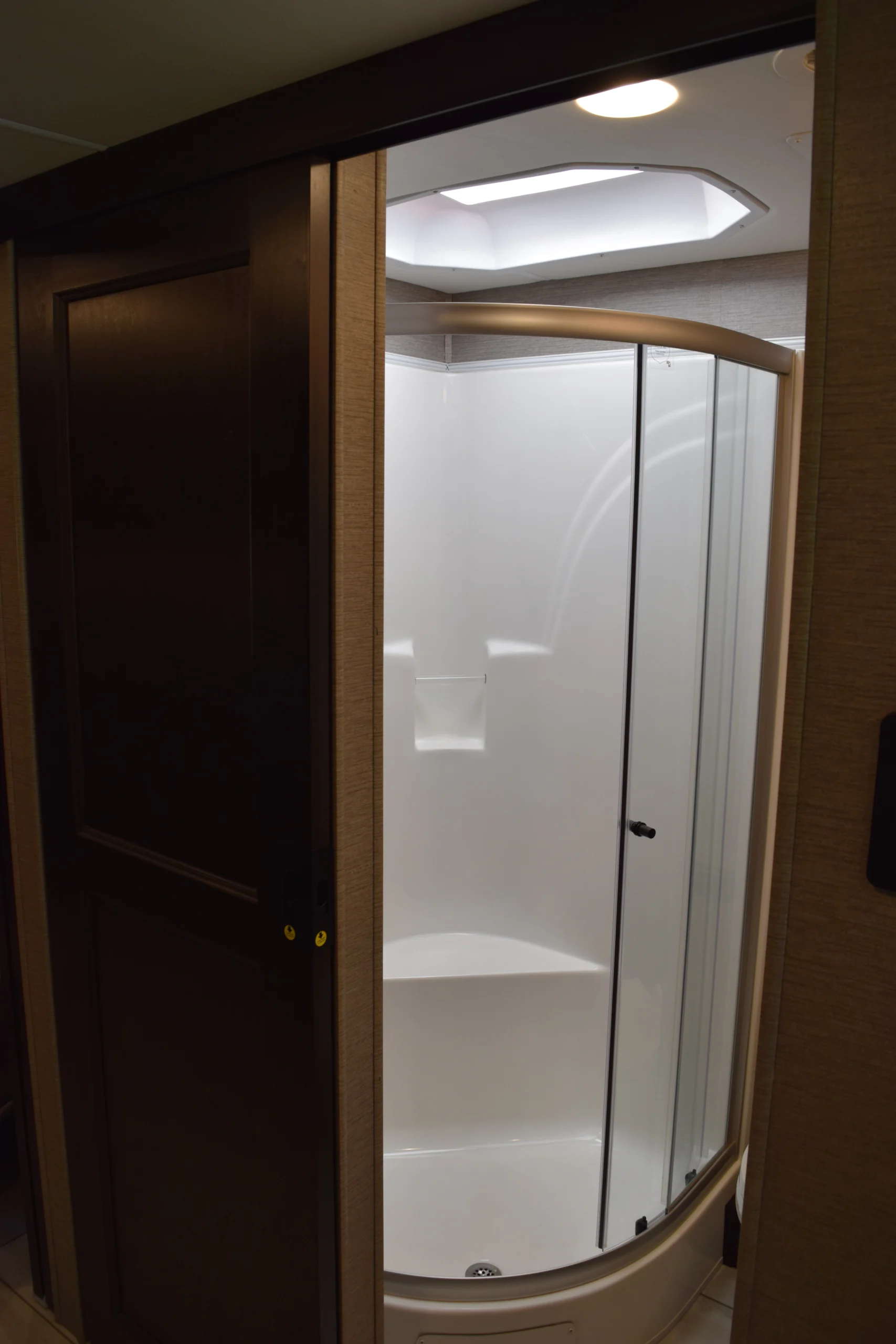 DSC_0756 RV bathroom with a frosted glass shower door, curved enclosure, and overhead light in motorcoach interior.