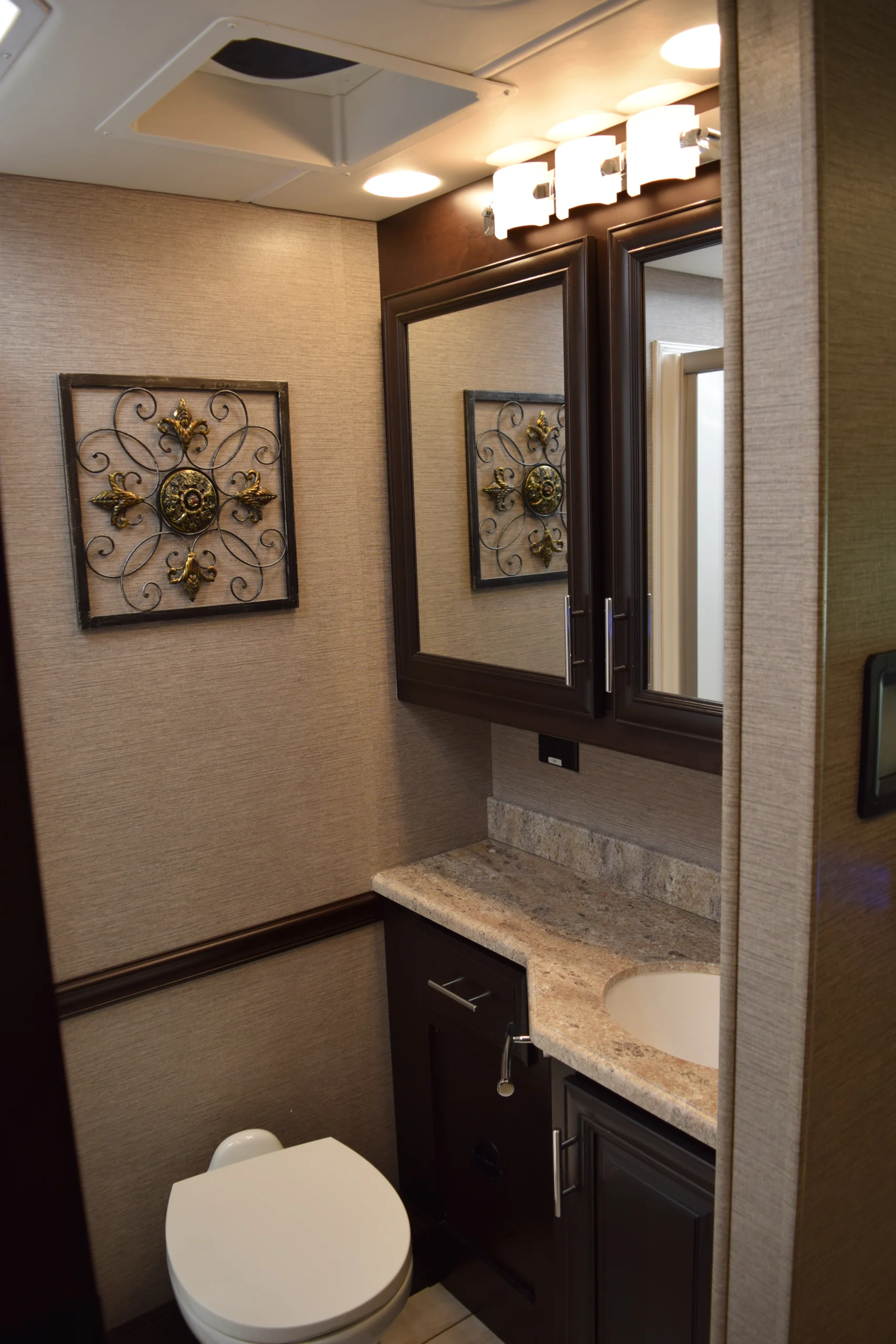 DSC_0757 Elegant Motorcoach and RVs bathroom with decorative artwork, granite countertop, dark wood cabinetry, and soft overhead lighting.