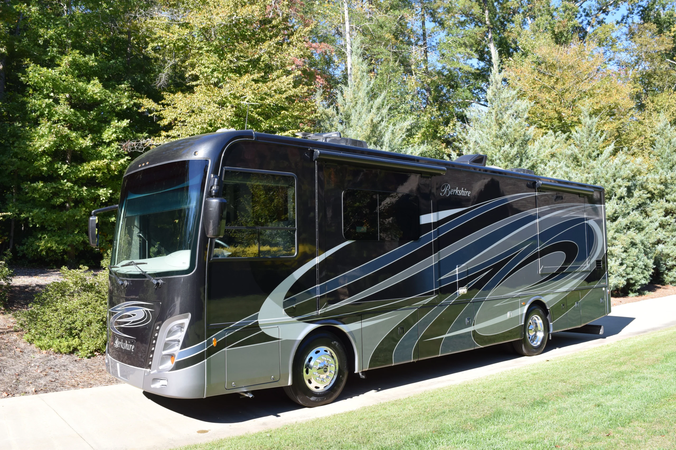 DSC_0765 Black Berkshire motorcoach RV parked on a driveway, surrounded by lush green trees and bushes.