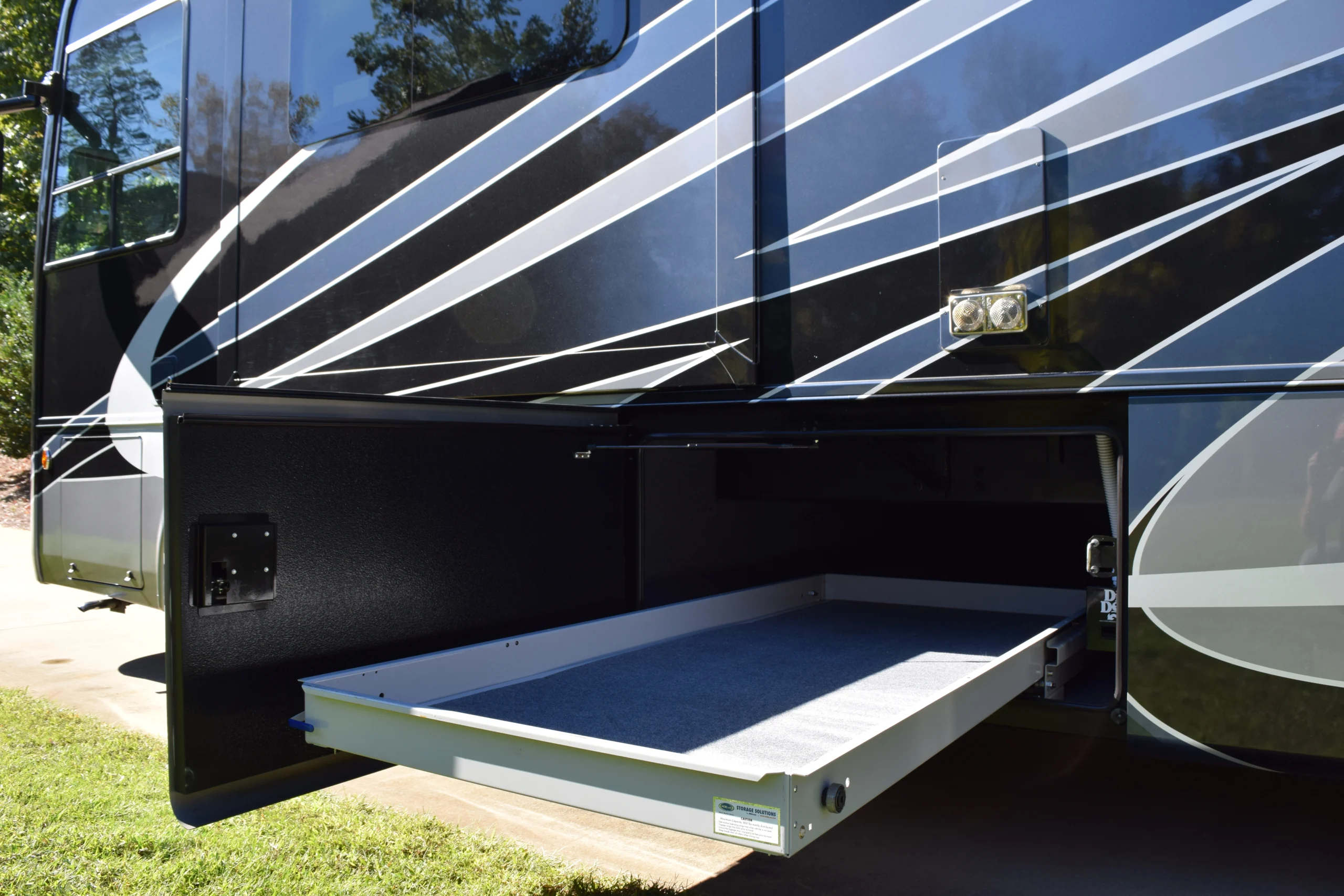DSC_0768 Motorcoach and RV storage compartment with sliding tray extended, showcasing sleek, modern exterior design with white stripes.