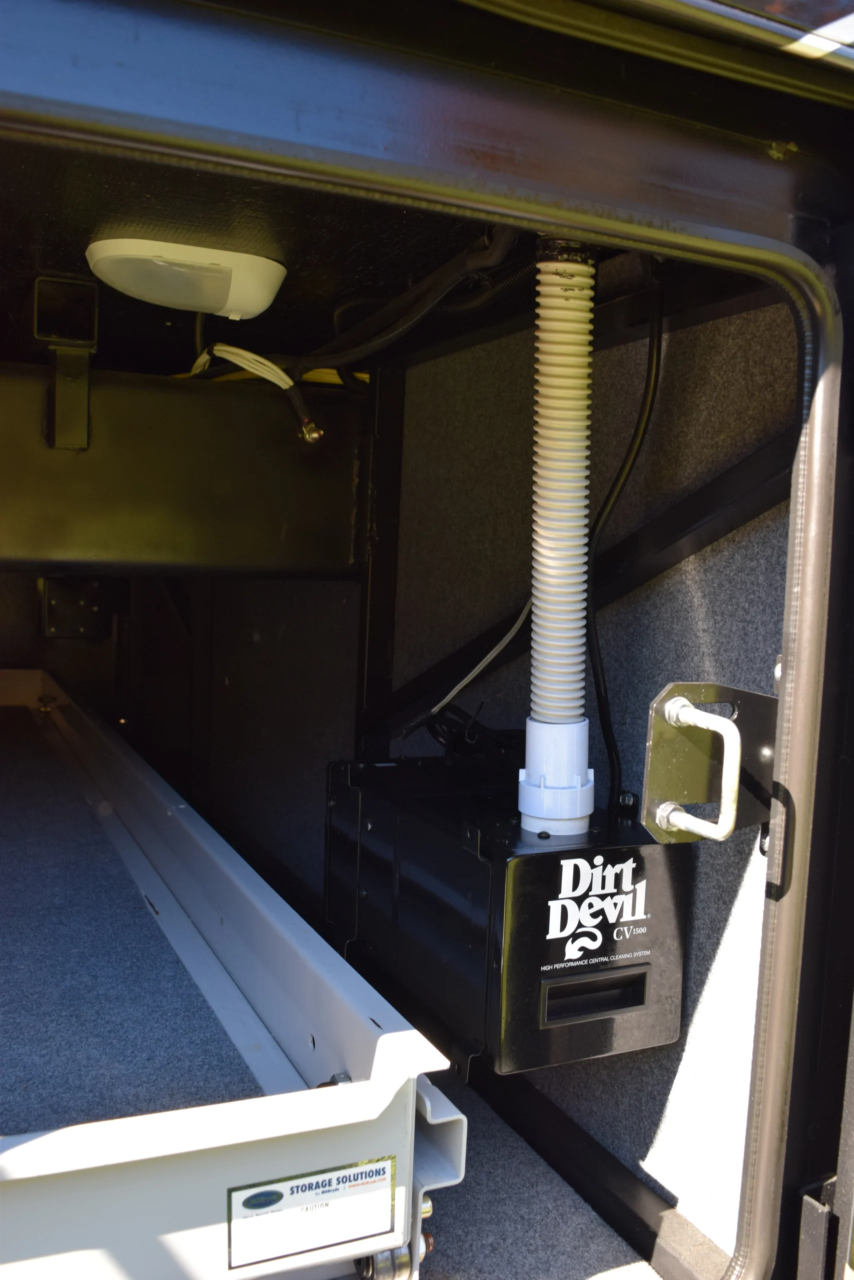 DSC_0769 Storage compartment in an RV with a mounted Dirt Devil CV1500 central vacuum system, featuring a white hose.