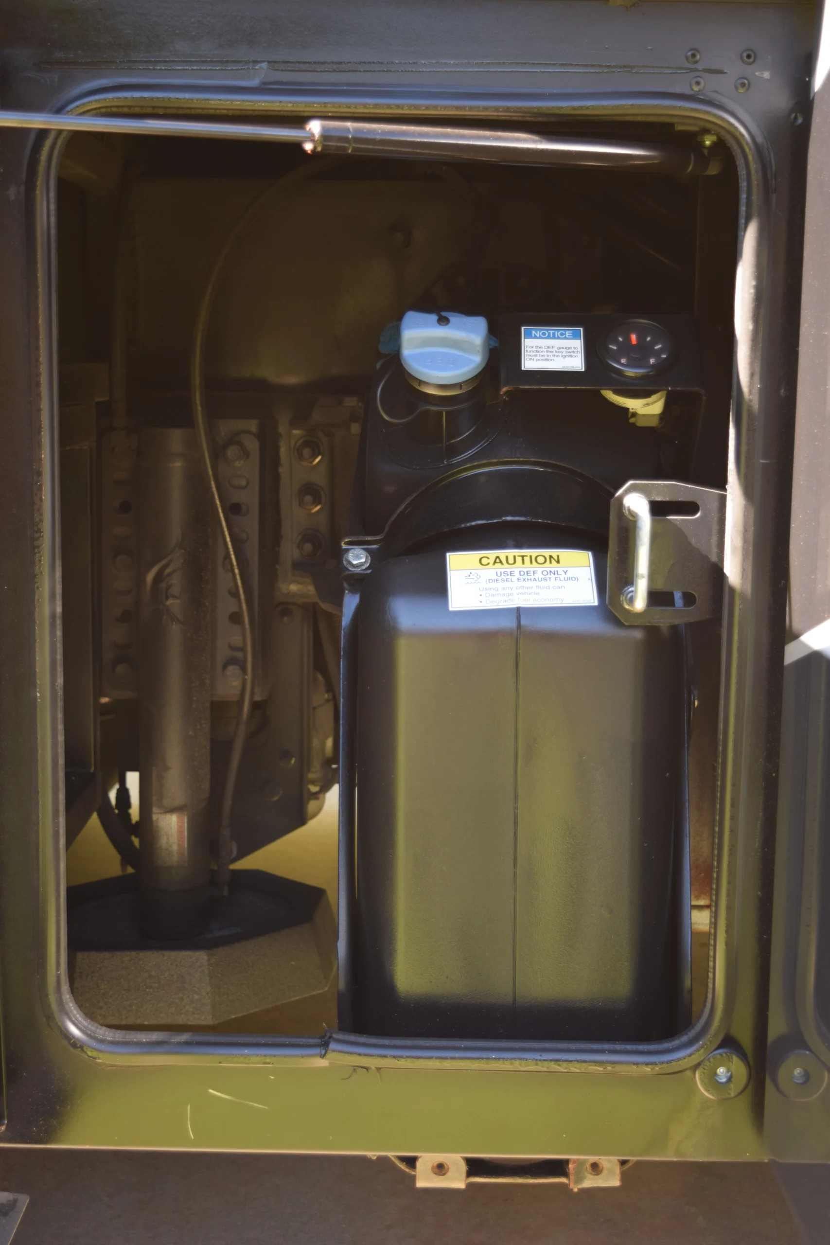 DSC_0772 DEF tank compartment in a motorcoach, labeled with caution and notice signs, secured within the vehicle's cabin.