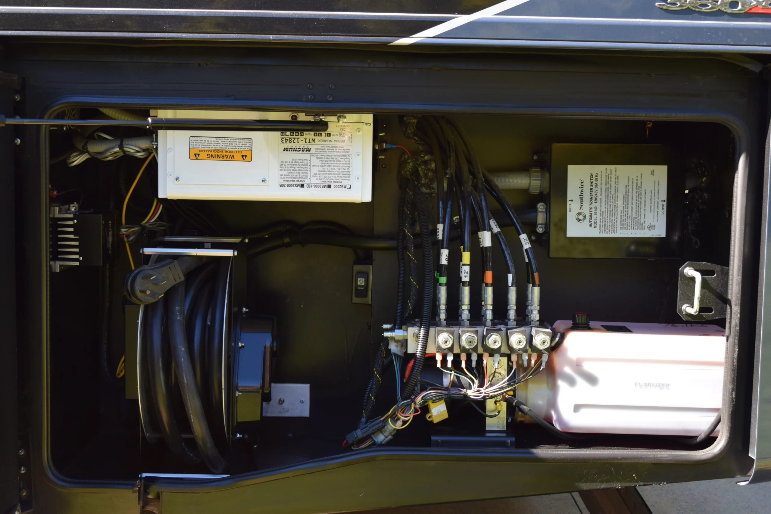 DSC_0773 Motorcoach and RVs service panel with coiled cables, labeled connectors, and electrical components inside an access compartment.