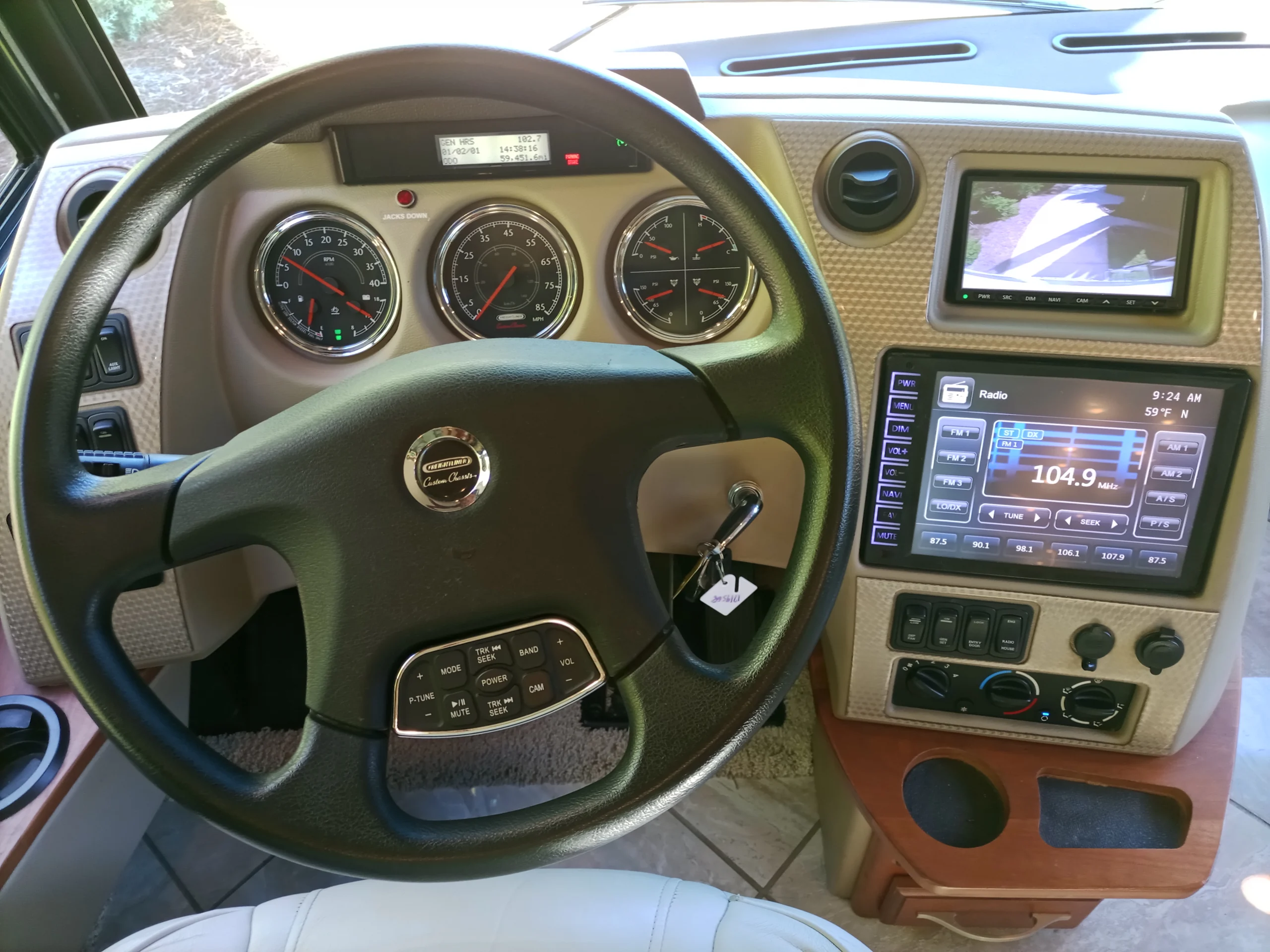IMG_20260928_092359_249 Motorcoach dashboard with steering wheel, speedometers, screens showing radio settings, and rear-view display.