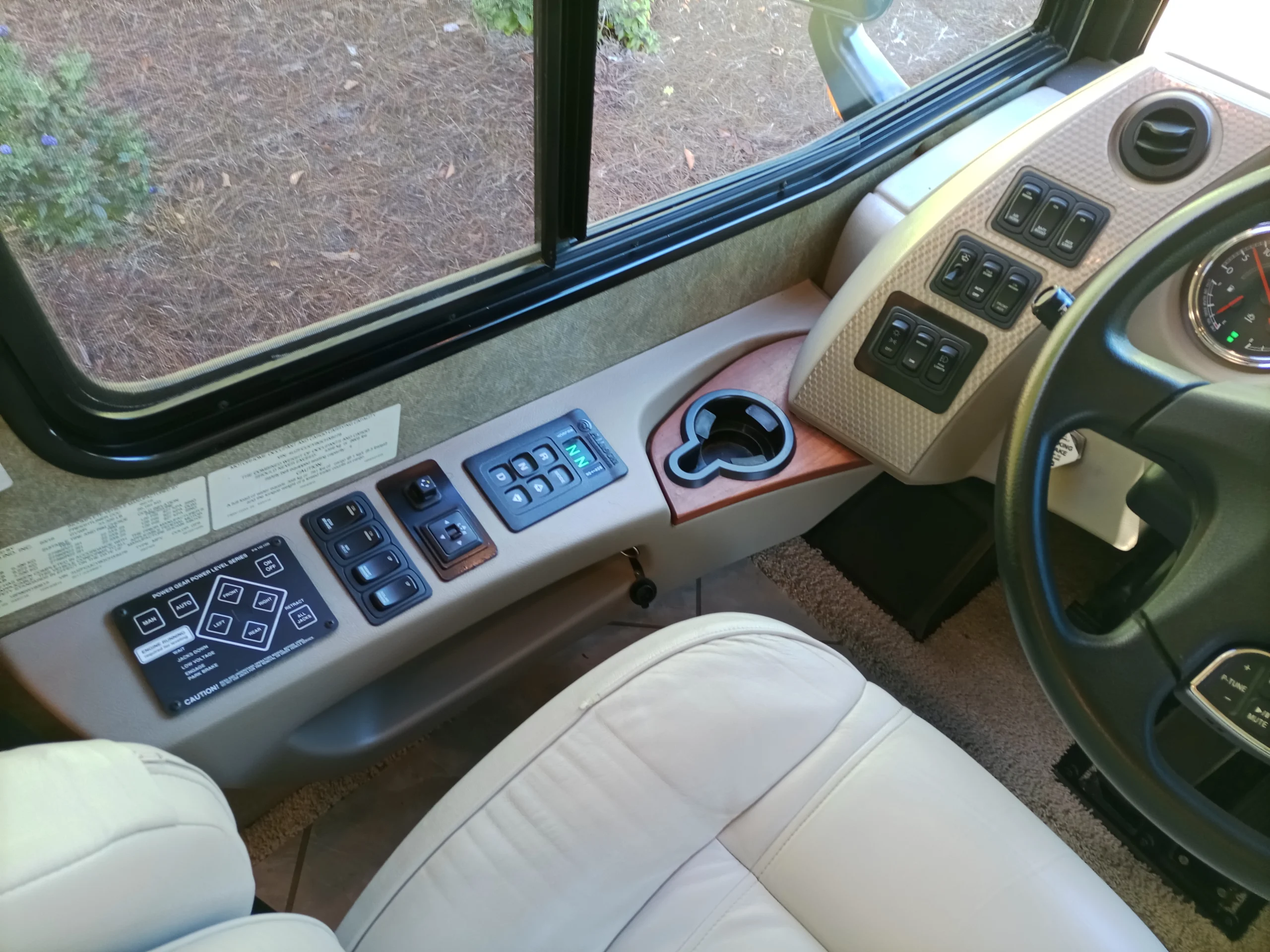 IMG_20260928_092416_166 Motorcoach driver’s seat with control panel, cup holder, and steering wheel in front. Various switches and buttons visible.