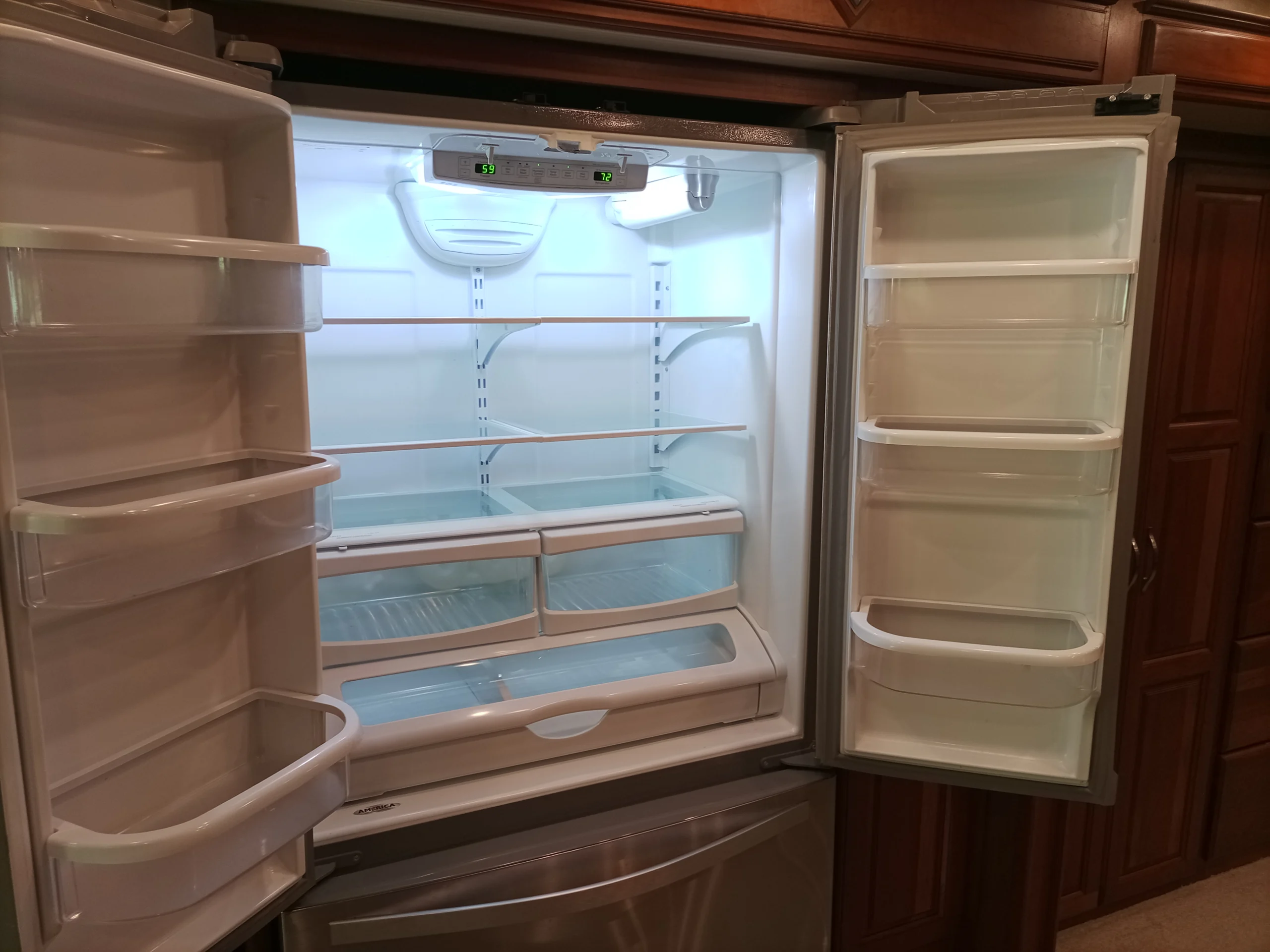 IMG_20260928_092800_858 Open, stainless steel double-door refrigerator in a Motorcoach and RVs kitchen, showing empty shelves and interior lighting.