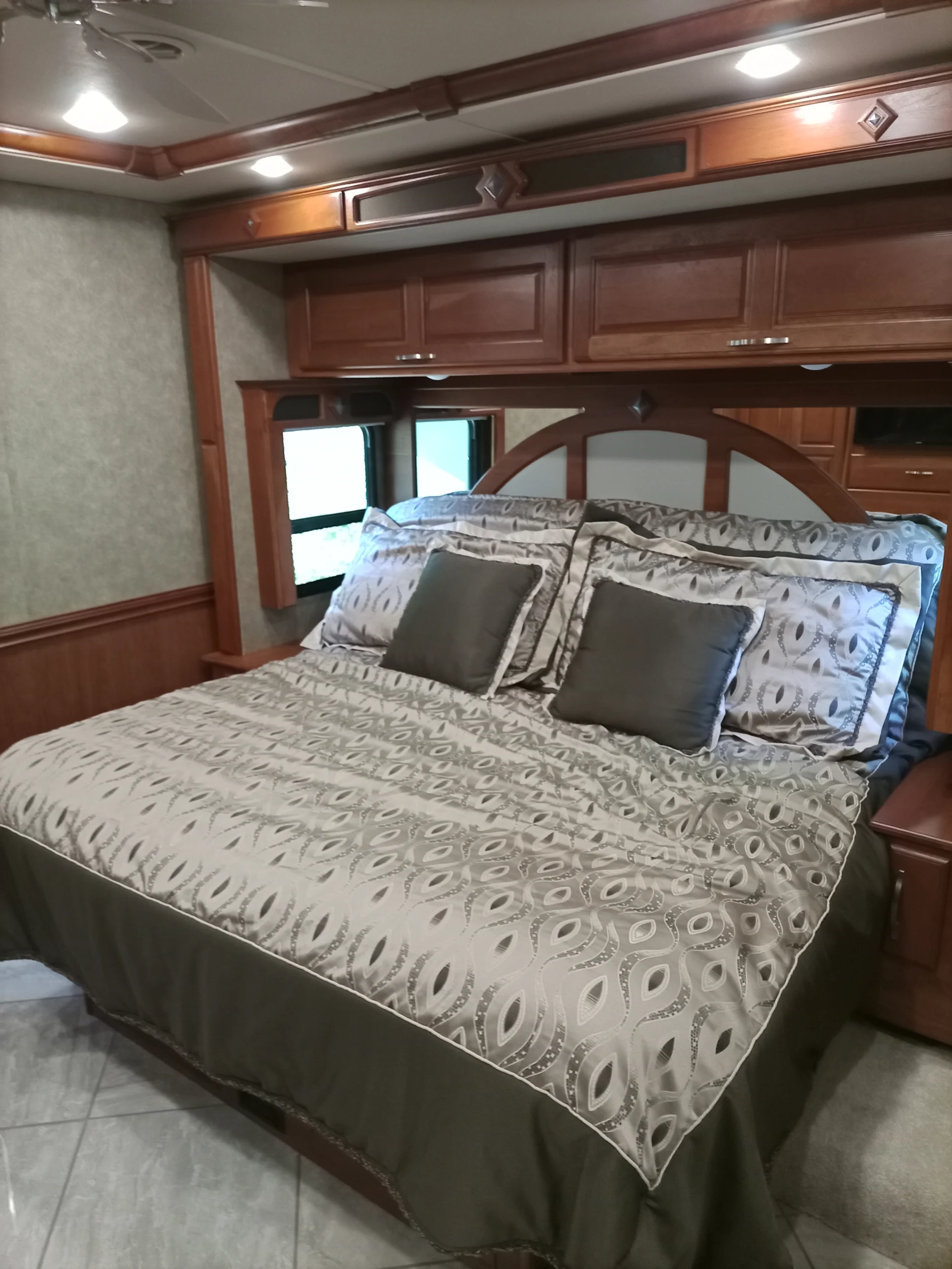 IMG_20260928_093138_328 Cozy RV motorcoach bedroom with patterned bedding, wooden cabinets, and soft lighting.