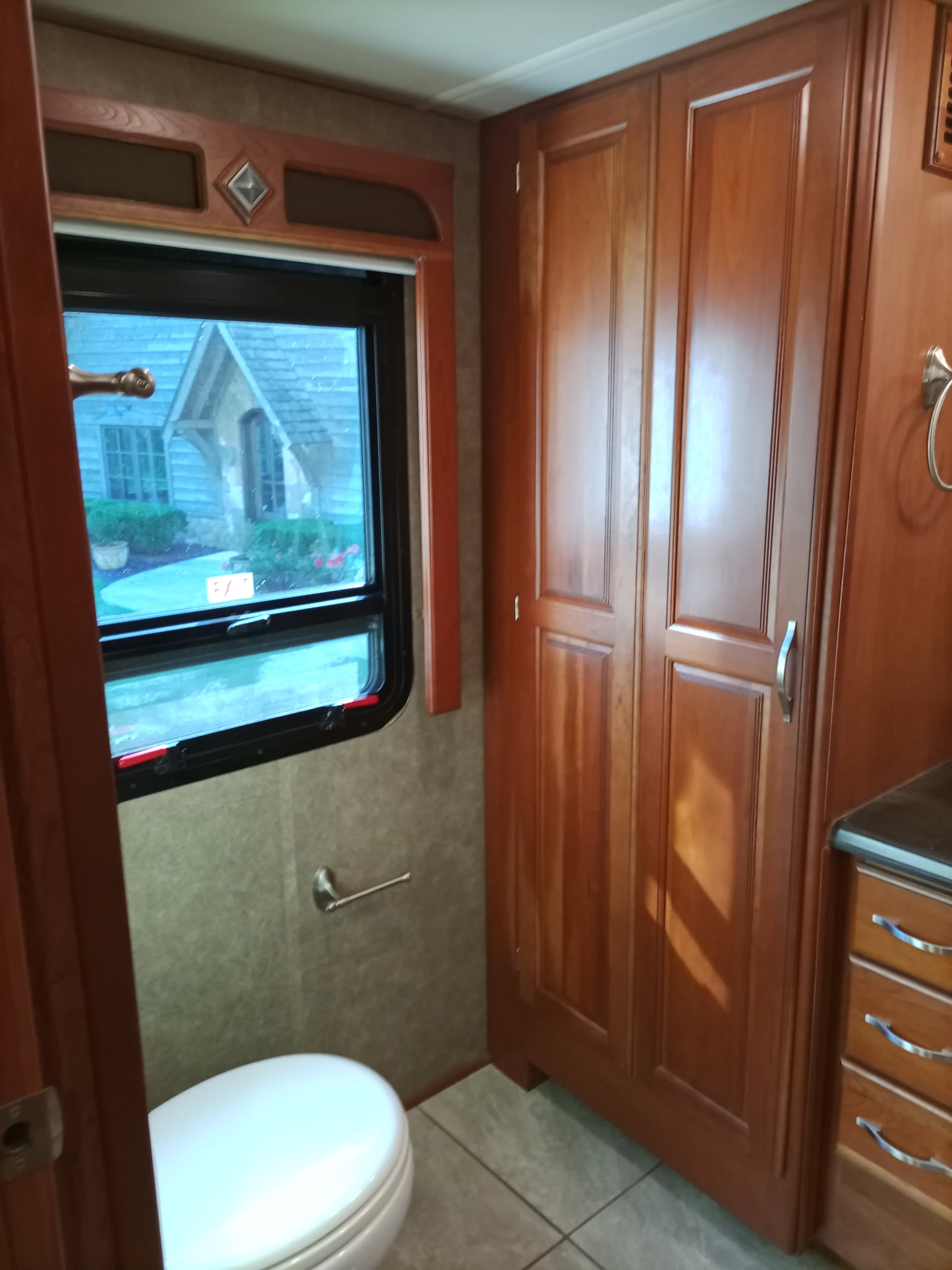 IMG_20260928_093151_444 Motorcoach and RVs bathroom with wooden cabinetry, tiled floor, window view, and toilet.