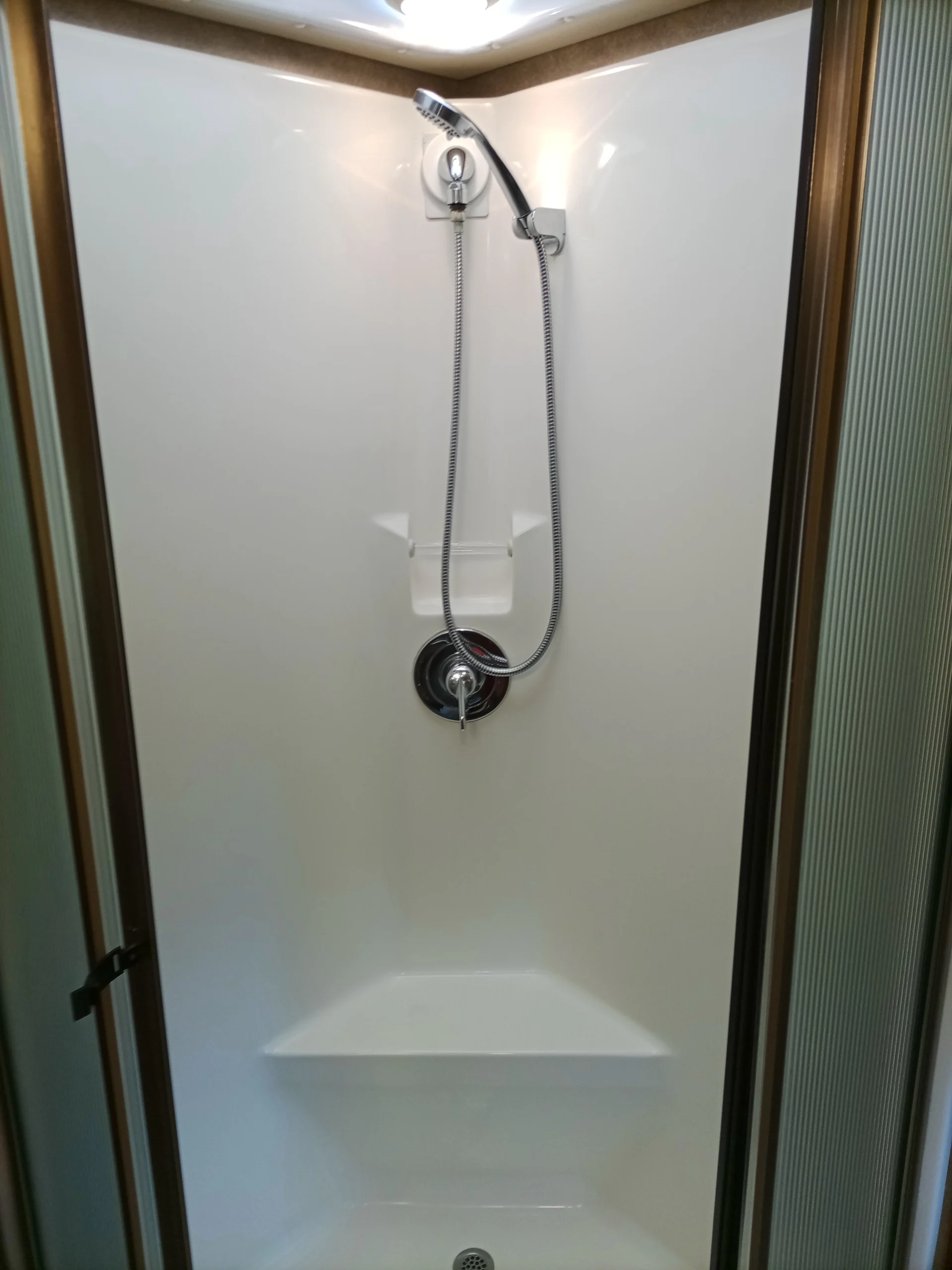 IMG_20260928_093234_581 Compact motorcoach shower with adjustable handheld showerhead, built-in shelf, and white walls, suitable for RVs.