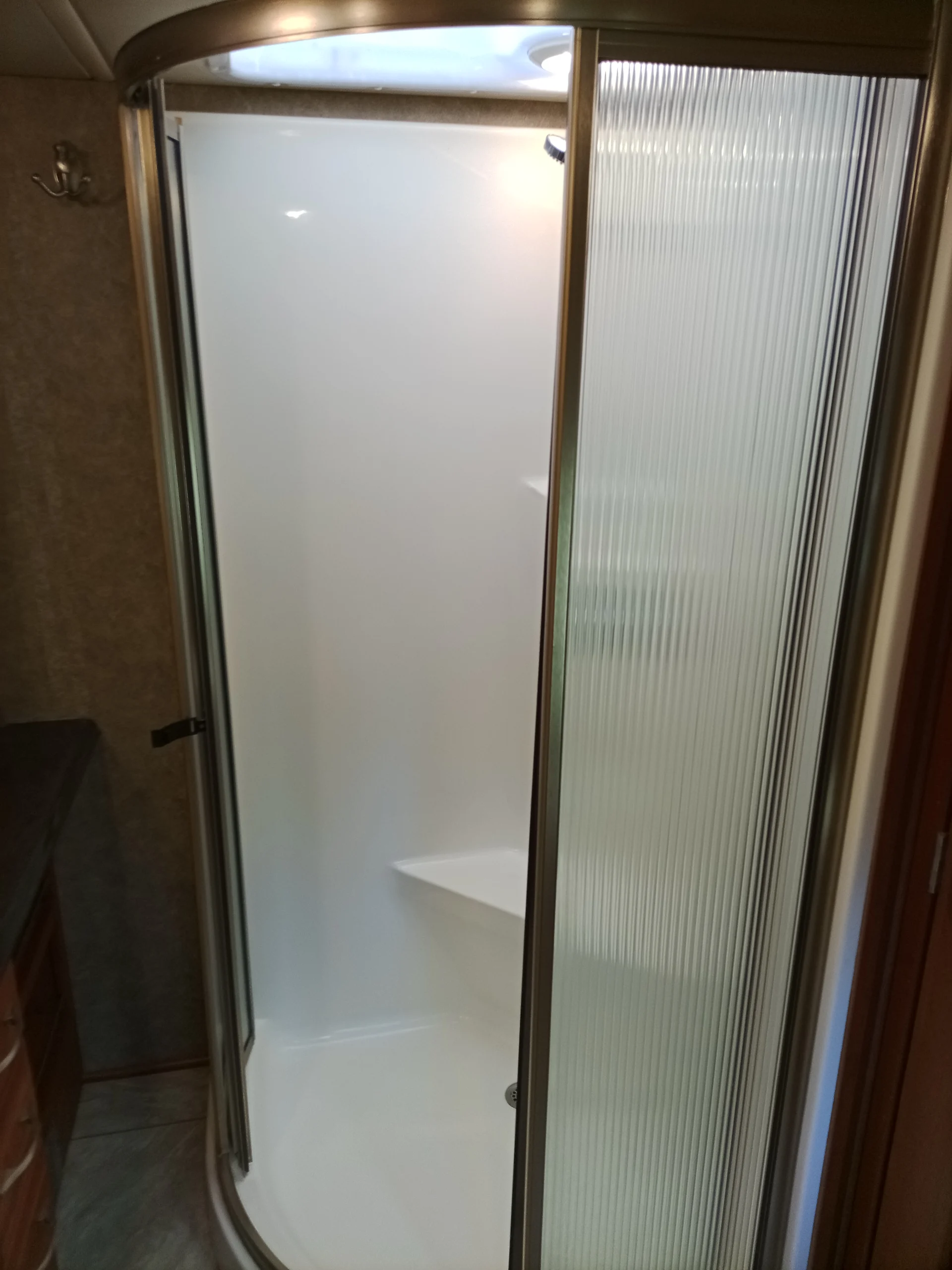 IMG_20260928_093240_114 Enclosed shower with clear sliding doors in a Motorcoach RV bathroom, featuring a white interior and built-in seat.