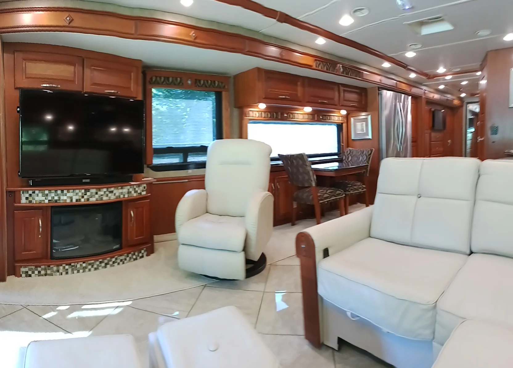IMG_20260928_093432_1 Luxurious motorcoach interior with leather seating, dining area, large TV, and modern kitchen appliances, emphasizing spaciousness and comfort.