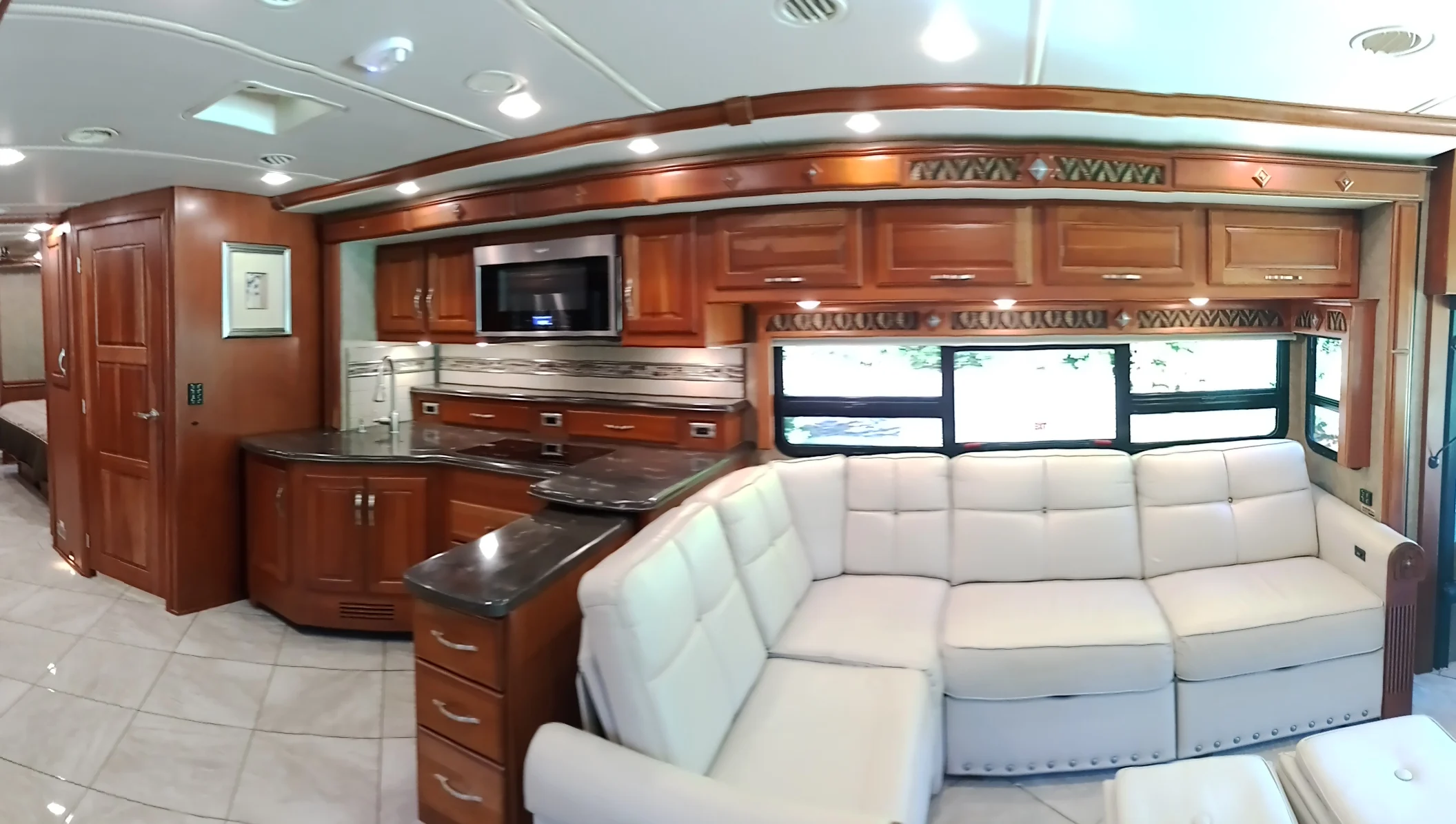 IMG_20260928_093543_9 Spacious Motorcoach and Rvs interior with plush white sectional sofa, wooden cabinetry, modern kitchen, and large windows.