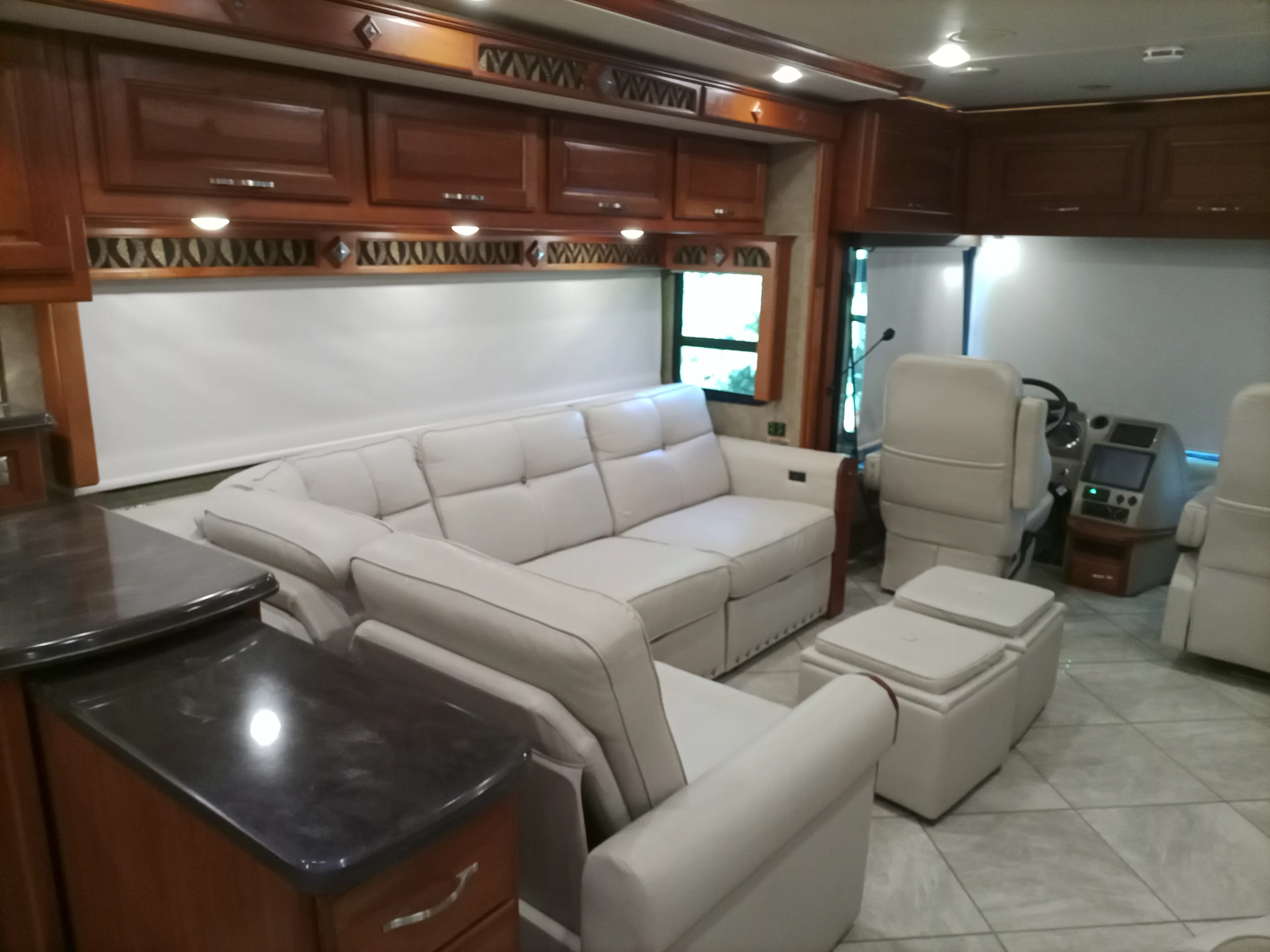 IMG_20260928_094112_226 Luxurious Motorcoach interior featuring white leather seating, polished wood cabinets, tiled floor, and a front driver's area.