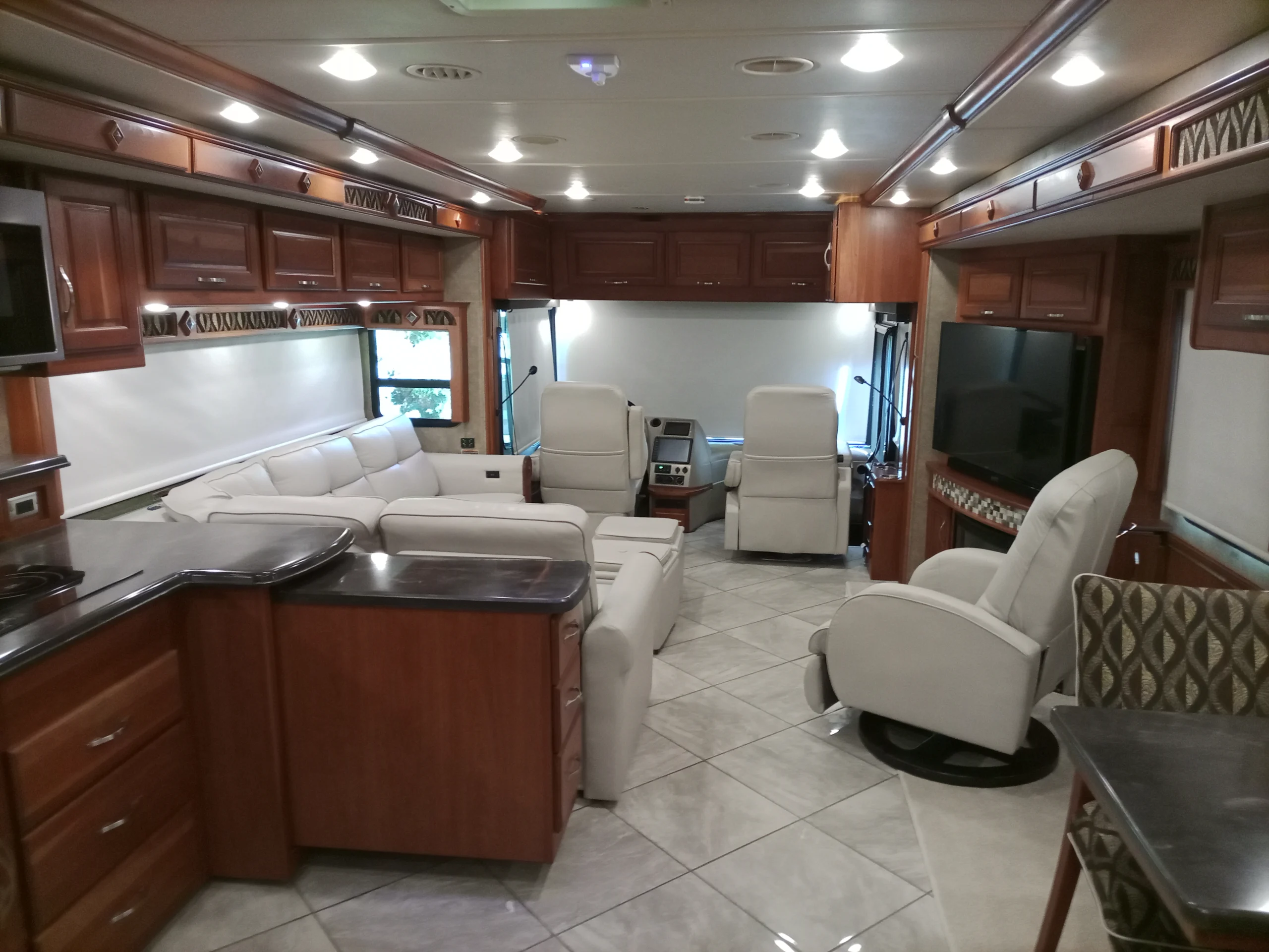 IMG_20260928_094120_393 Luxurious Motorcoach interior with plush seating, sleek cabinetry, tiled floor, large TV, and modern kitchen area, designed for comfort and style.