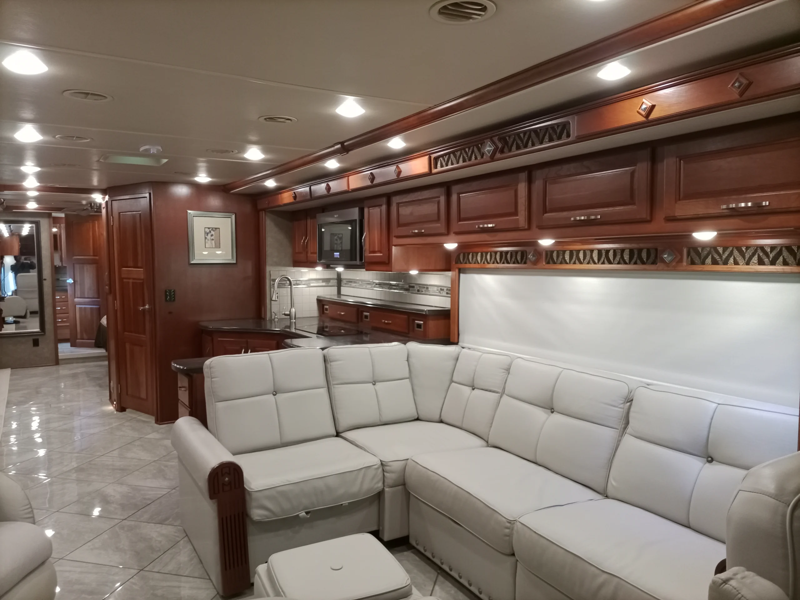 IMG_20260928_094214_595 Luxurious motorcoach interior with plush L-shaped sofa, wooden cabinetry, and modern kitchen, highlighting the elegance of RV living.