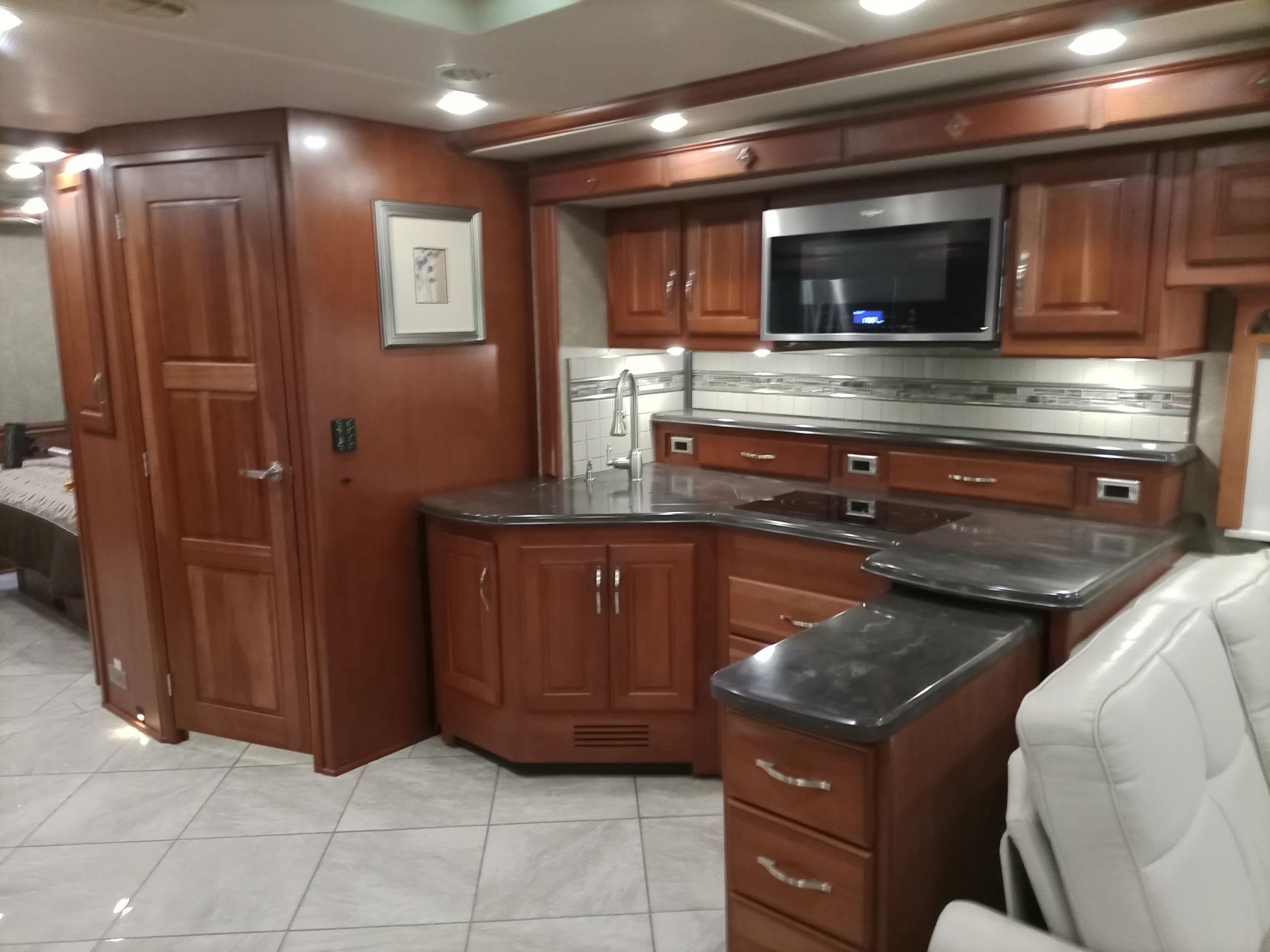 IMG_20260928_094244_934 Luxurious Motorcoach kitchen with cherry wood cabinets, granite countertops, built-in microwave, and tile flooring.