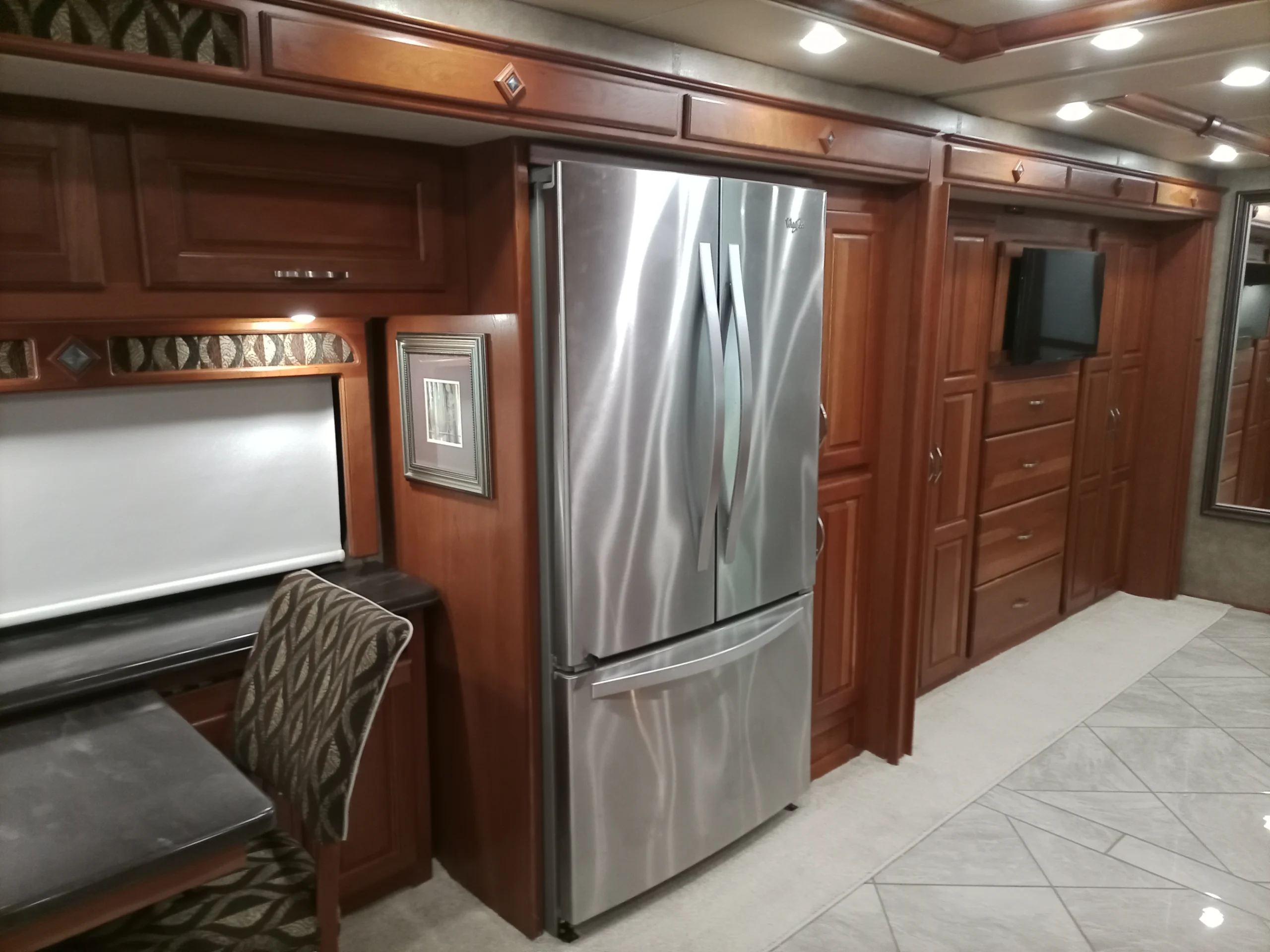 IMG_20260928_094307_700 Luxurious motorcoach interior with stainless steel fridge, wooden cabinets, and built-in TV, offering a spacious and upscale RV experience.