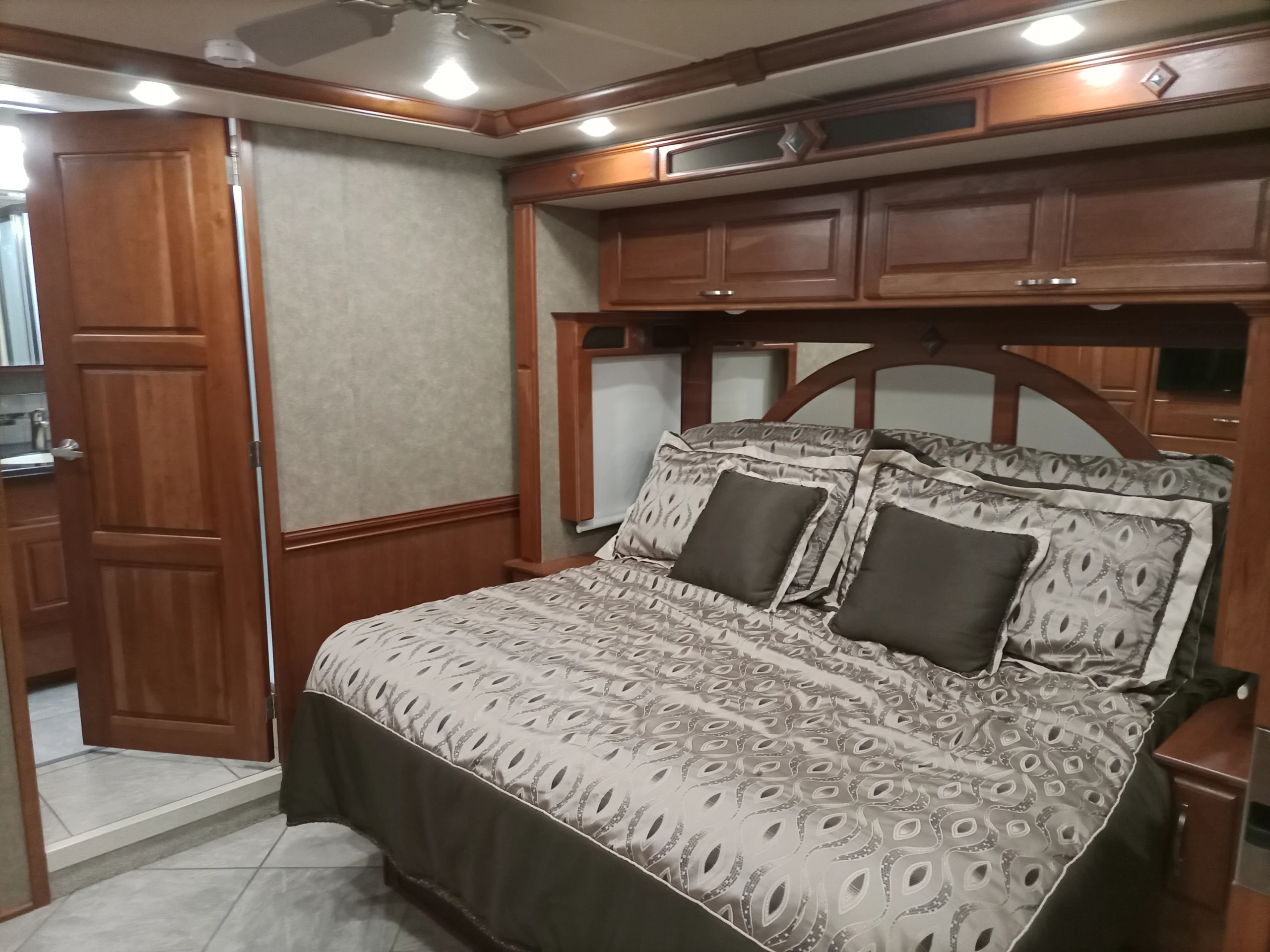 IMG_20260928_094445_181 Cozy RV bedroom with a patterned bedspread, wooden cabinets, and a glimpse of the bathroom, perfect for Motorcoach and RVs living.