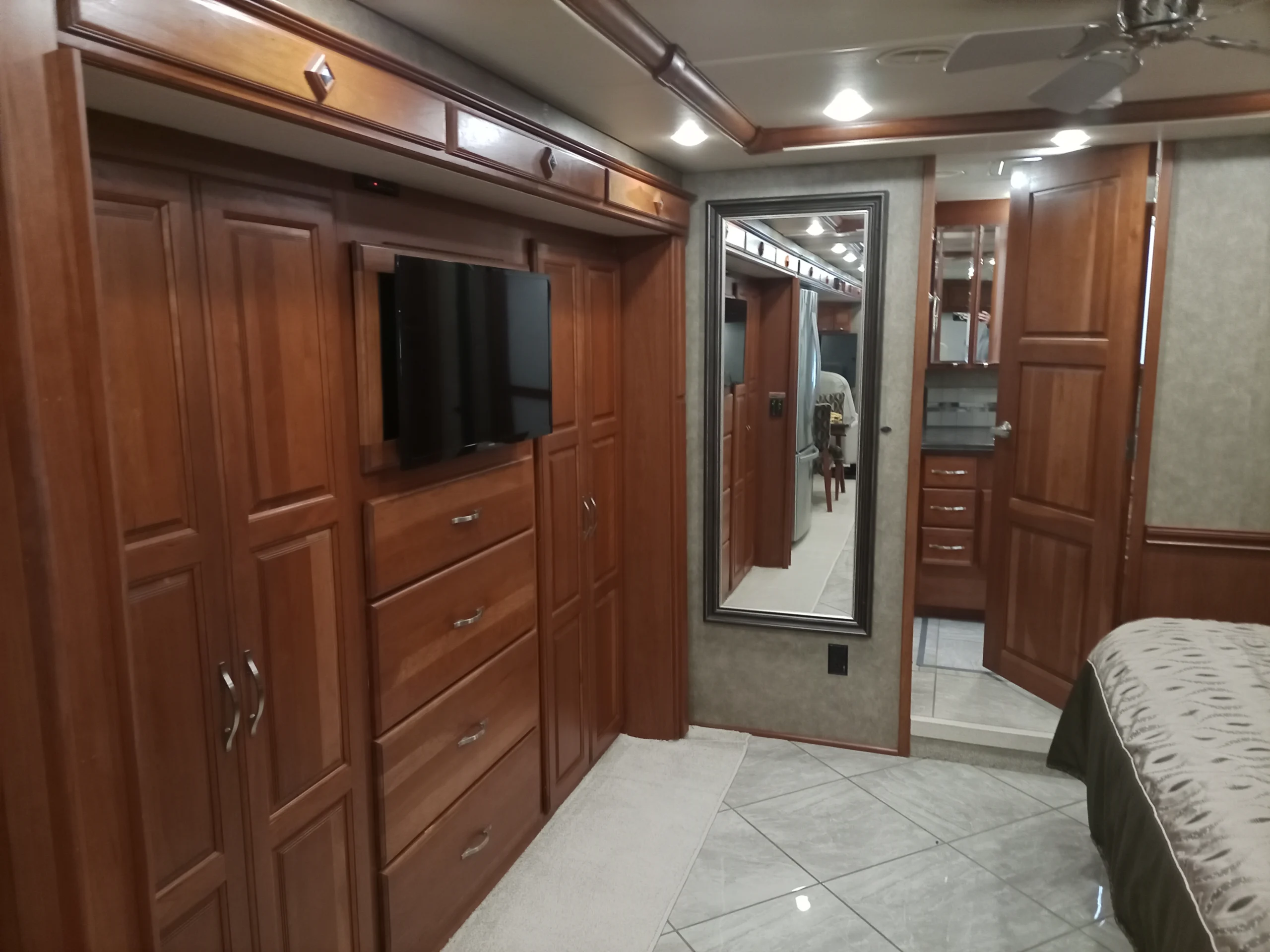 IMG_20260928_094452_146 Luxurious Motorcoach and RV interior with wooden cabinets, a mounted TV, a mirrored wall, and plush bedding, conveying comfort and elegance.