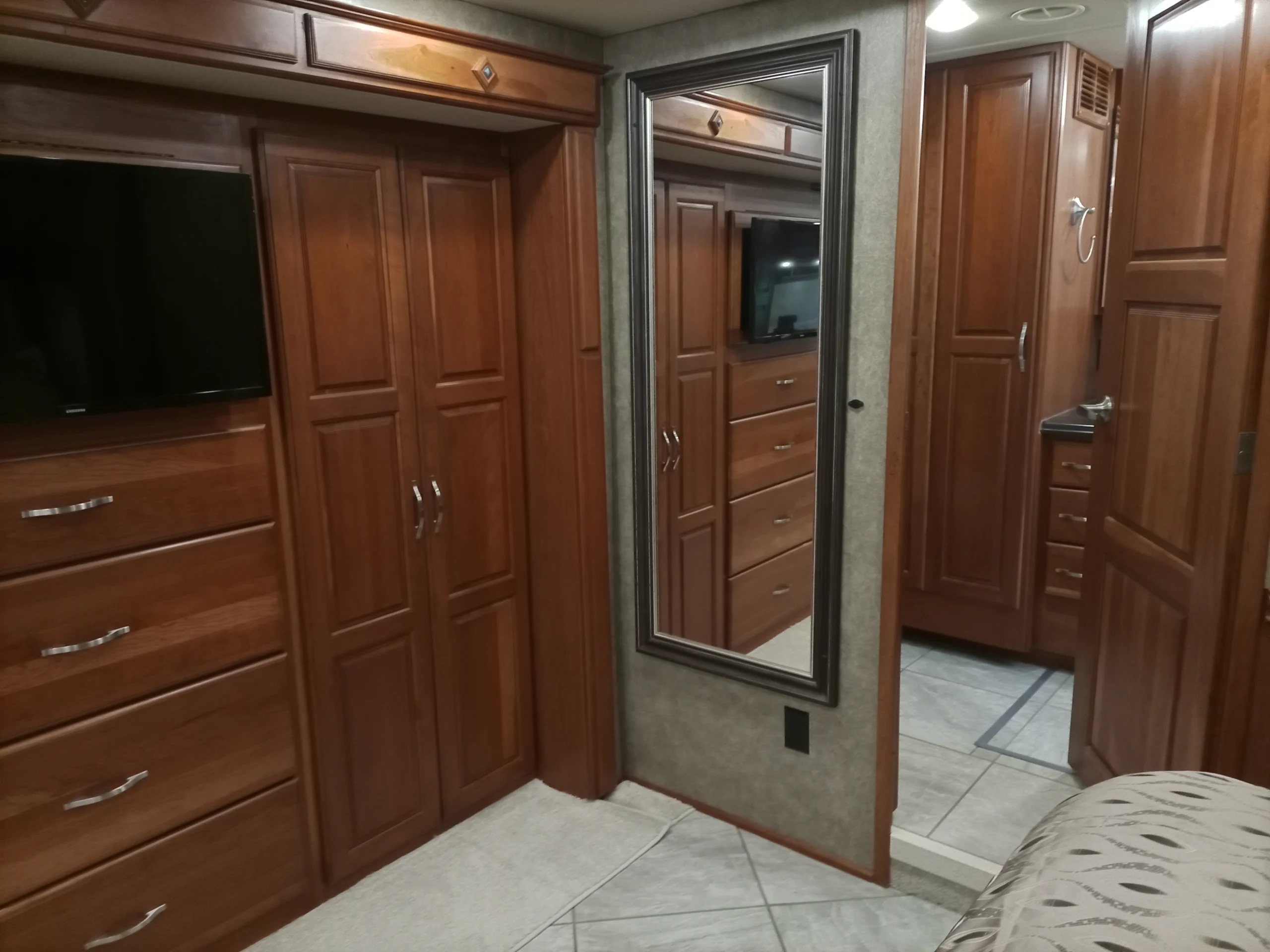 IMG_20260928_094503_686 Motorcoach RV interior featuring wood cabinets, drawers, wall-mounted TV, and a tall mirror, providing a cozy and functional living space.