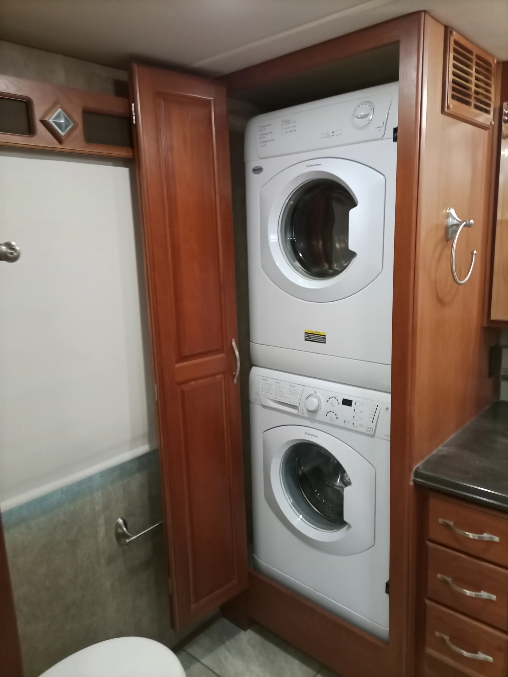 IMG_20260928_094518_894 Stacked washer and dryer in wood cabinet within a Motorcoach and RVs bathroom, next to toilet and drawers.