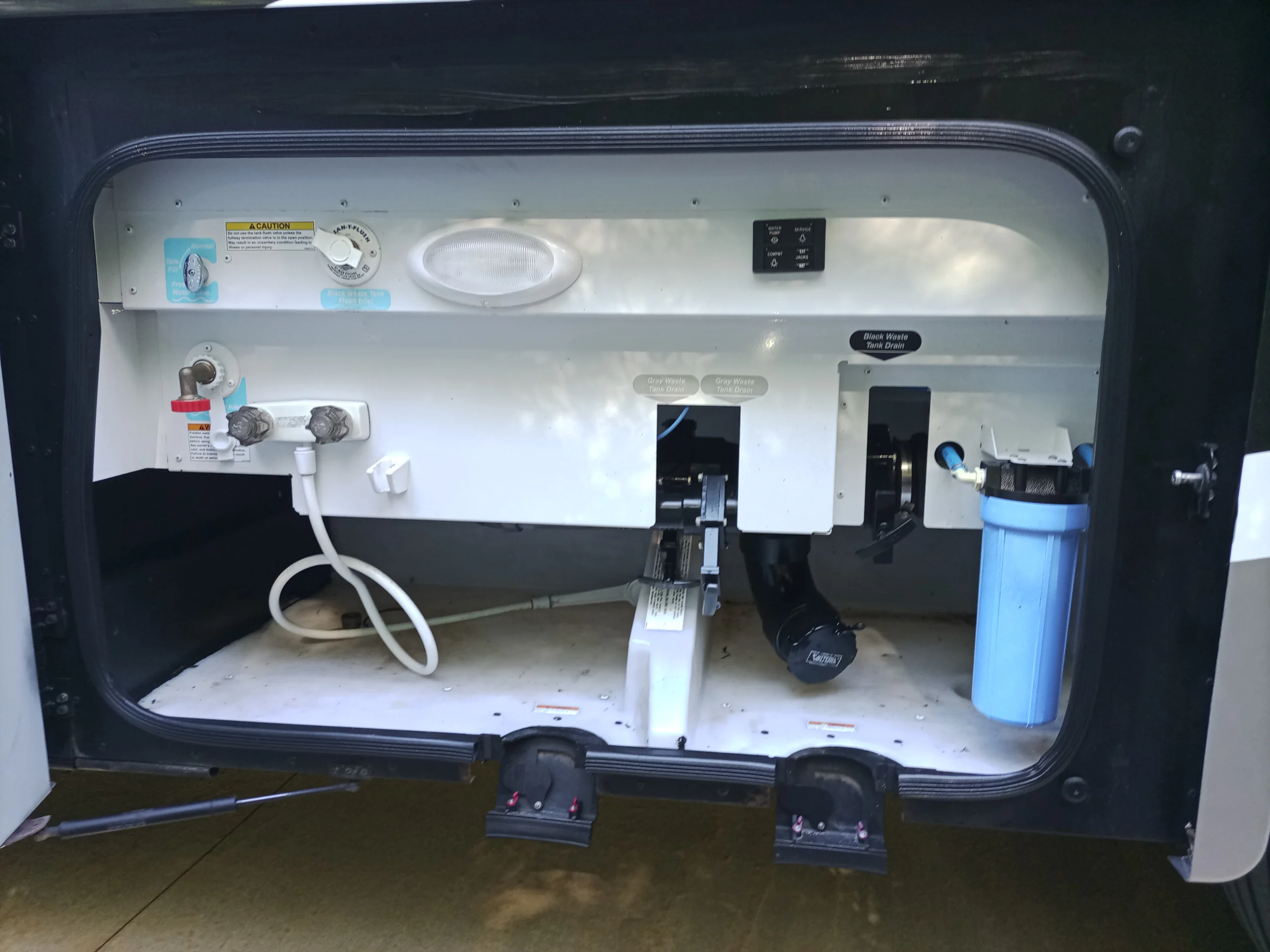 IMG_20260928_160238_728 RV service compartment showing water connections, waste tank drains, filter, and control panel, essential for Motorcoach and RV maintenance.